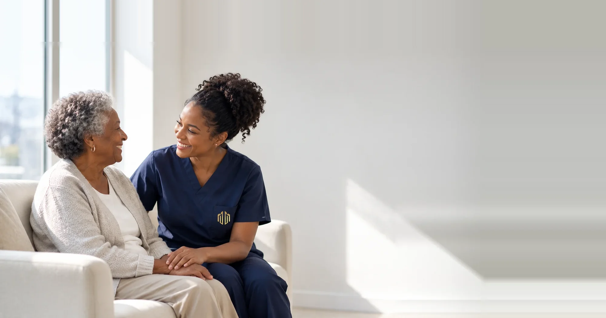 A caregiver sitting with a resident in a bright, sunlit lounge